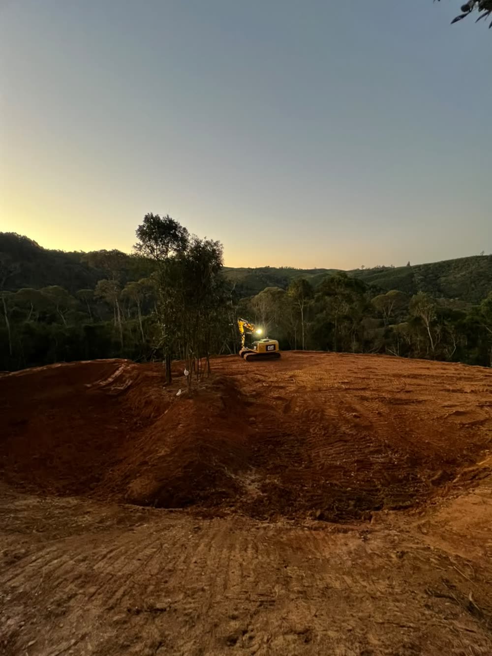 Escavadeira Caterpillar 312D com farol aceso, trabalhando ao entardecer